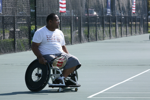 A man in a wheelchair prepares to play tennis